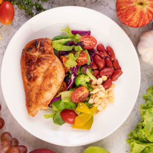 chicken-steak-topped-with-white-sesame-peas-tomatoes-broccoli-pumpkin-white-plate